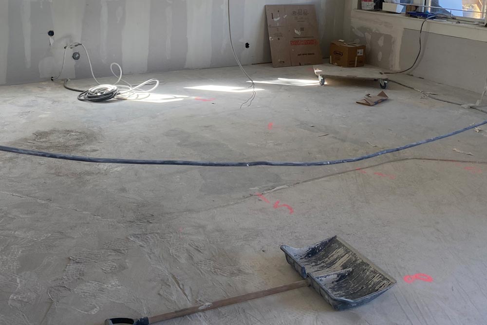 Betonggolv med sladdar och en stor spade i förgrunden, innan golvinstallationen påbörjats