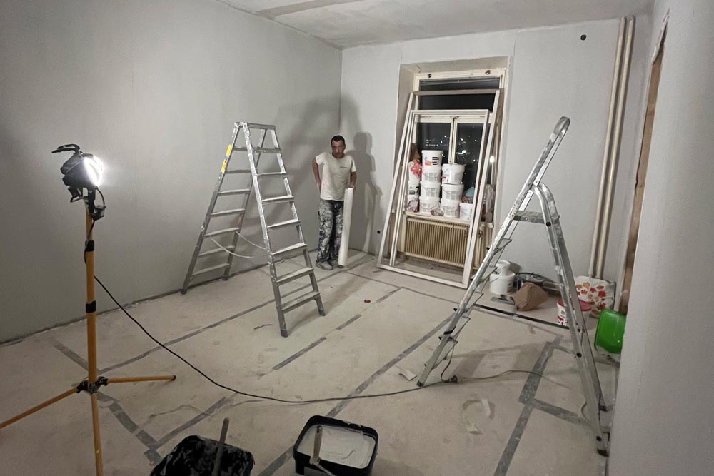 Rum under renovering med verktyg och två stegar, med en medarbetare i bakgrunden
