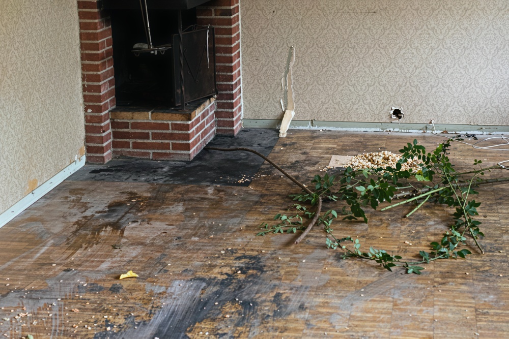 Slitet och smutsigt golv innan renovering, med vedspis i hörnet i bakgrunden och äldre tapet på väggarna