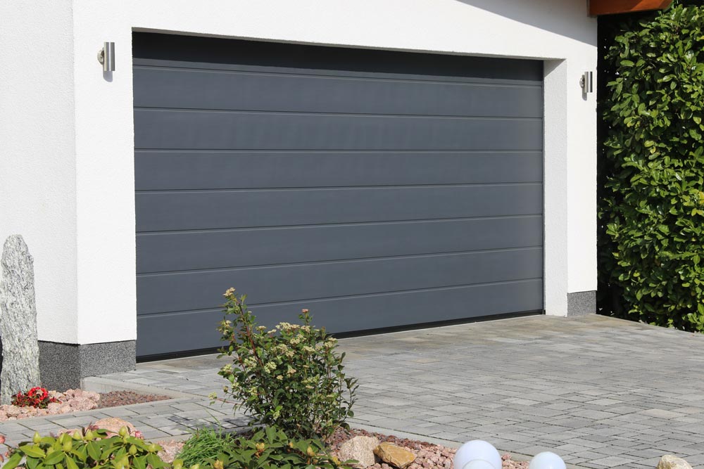 Modern, vit garagetillbyggnad med en grå garageport